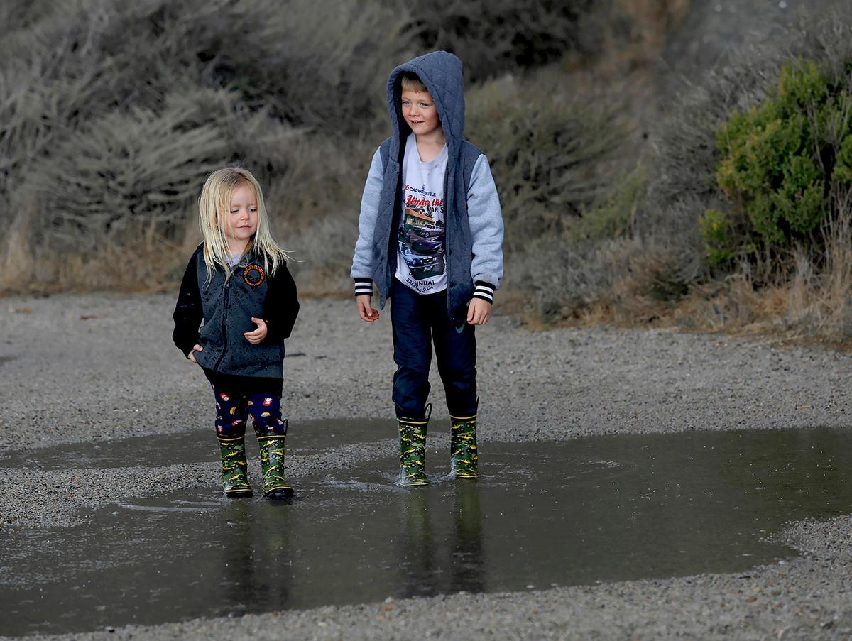 Two brothers, Harlin Lankford, 3 , left and Hazen Lankford, 7, of Morro Bay, play in a puddle in the rain near Morro Rock after watching the big waves. A rain storm brought high surf and big waves to the Morro Bay Harbor breakwater on Wednesday, Nov. 27, 2019.