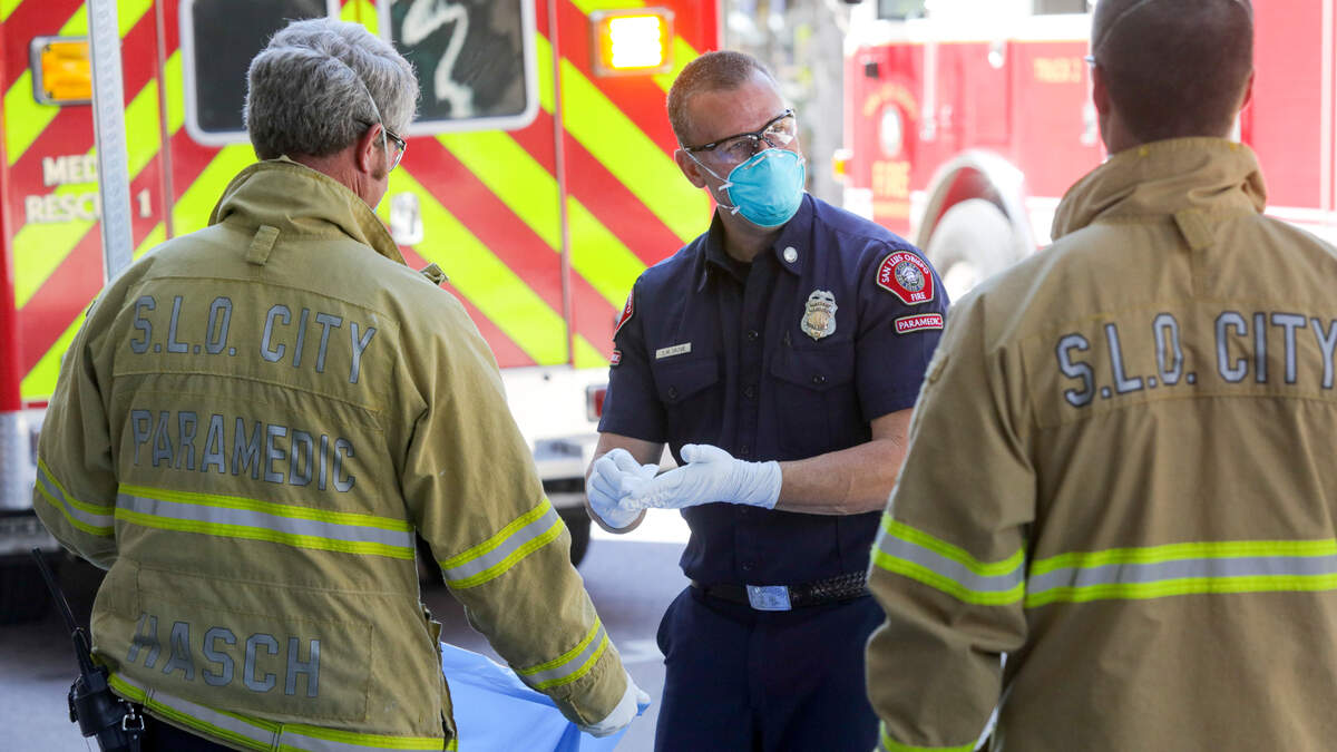 San Luis Obispo city Fire Captain Shayne Skove performs the cleaning protocol after helping someone exhibiting symptoms consistent with coronavirus in March 2020. Other firefighters are ready to dispose of used protective equipment.