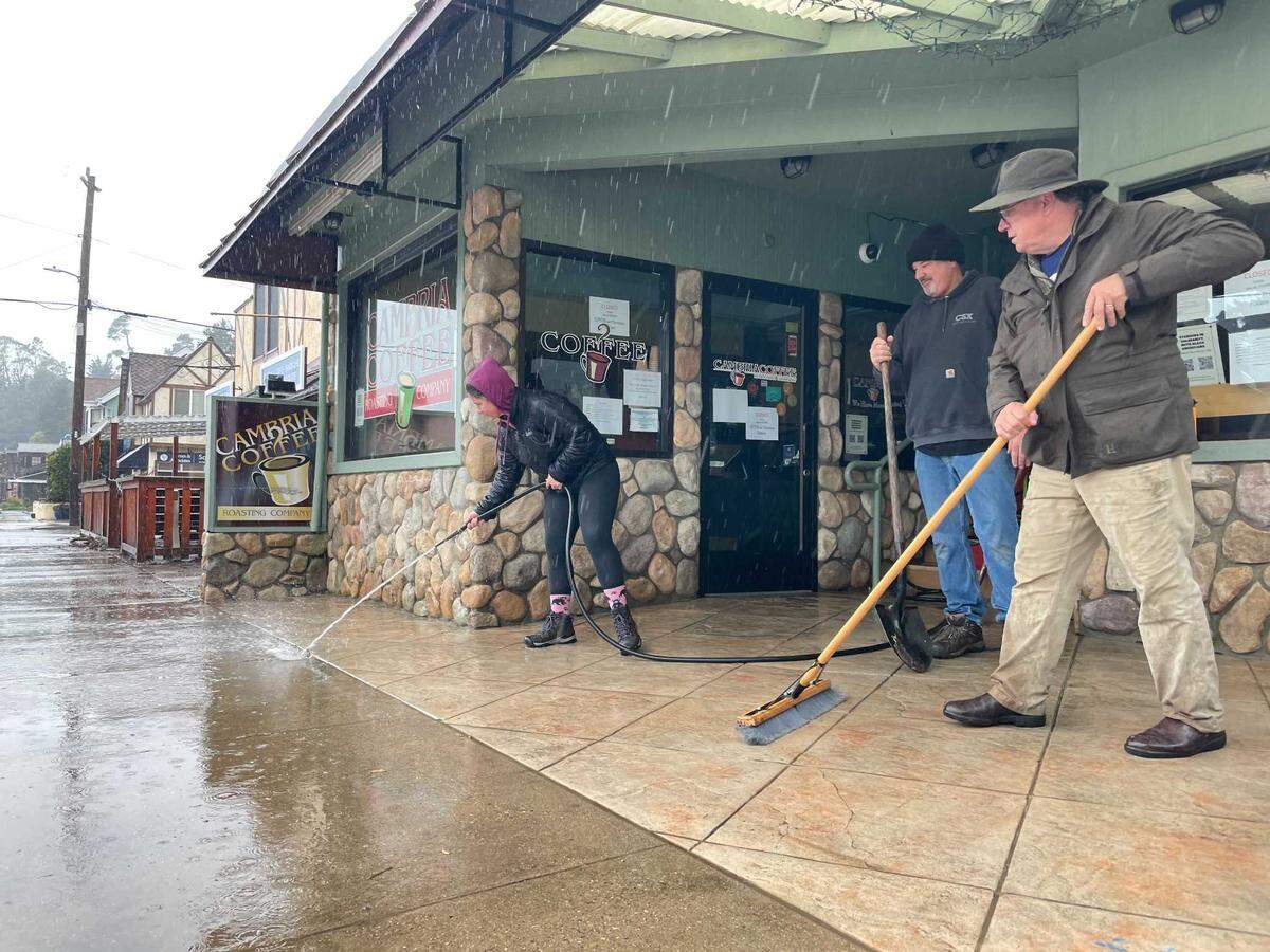 Tom Walsh, in the black beanie, and two other Cambria residents help clear water from in front of the Cambria Coffee Roasters Company. Walsh, who owns the coffee shop, said water had overflowed to the steps in front of the store by 10 a.m. Wednesday.