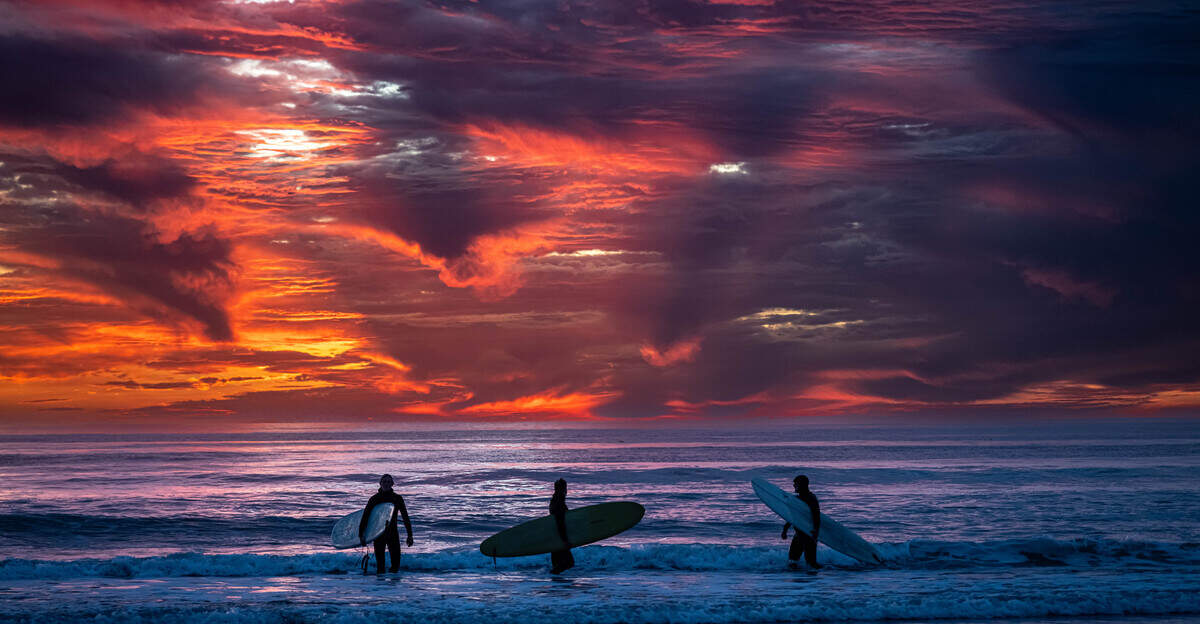 Surfers enjoy a beautiful sunset created by extensive mid-level clouds in San Luis Obispo County.