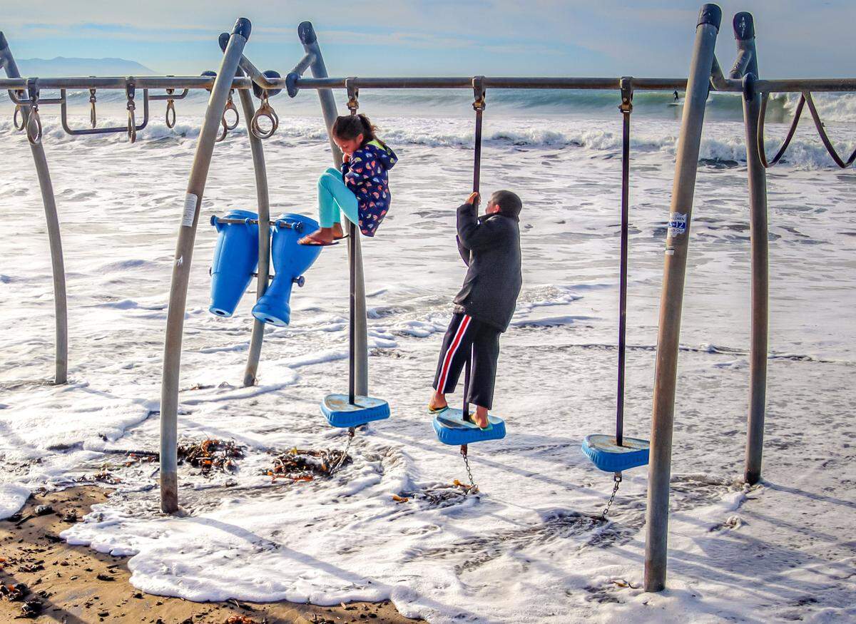 Maryanne and Anthony Tamayo use the swings to dodge the high tide while playing on the beach in Cayucos on Jan. 13. High tides combined with a coming storm could cause flooding in the coastal community on Jan. 27 and 28.