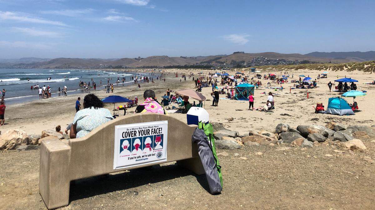 Crowds enjoy a warm day on the beach near Morro Rock in 2020. The city is considering a plan to bring paid parking to the lot.
