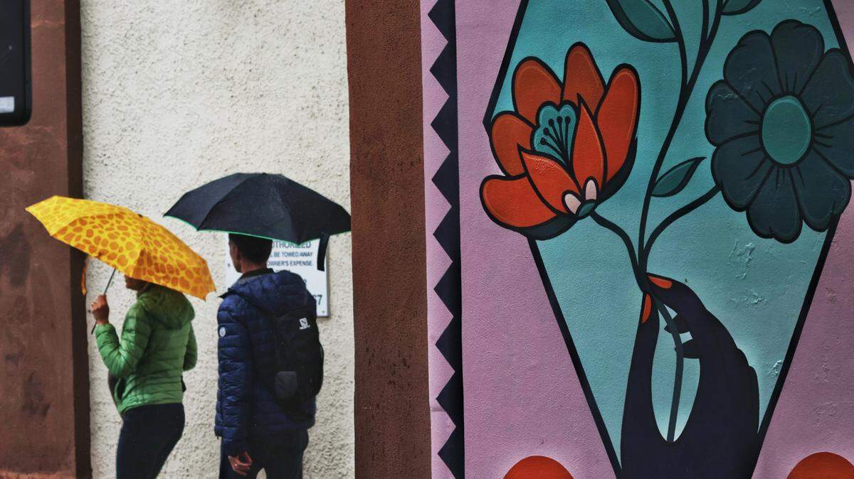 Rain falls in downtown San Luis Obispo as the first significant storm of 2022 arrives on March 25, bringing out umbrellas. Pedestrians walk near the mural on Marsh Street next to the Masonic Temple.