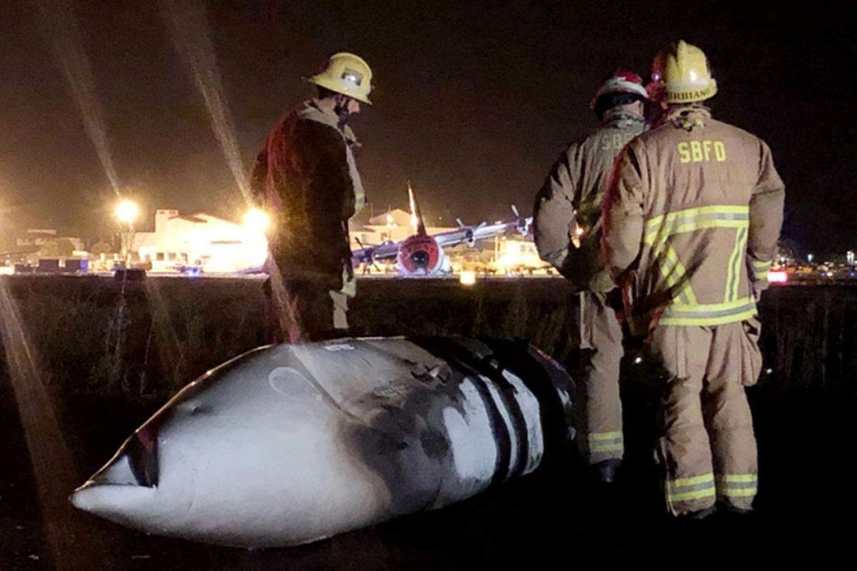 Firefighters examine a piece of wreckage that broke off of a C-130 aircraft that crashed late Sunday while attempting to make an emergency landing at the Santa Barbara Airport.