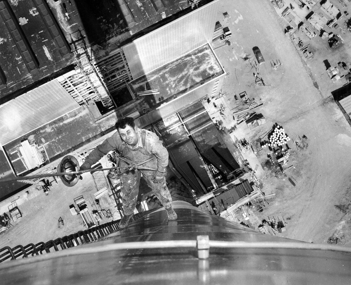 THE STACK IS HIGH...This dramatic photo of a rigger, Orval Ady, dangling 15 feet below the top of PG&E’s 450-foot smokestack was taken last March by Telegram-Tribune photographer Fen Truebridge who had just previously been hoisted up through the giant chimney’s brick-lined interior. The power plant building is shown at the top left. This picture was distributed nationally. From 7-7-1955 dedication edition of the Telegram-Tribune. The plant was dedicated the next day, 7-8-1955. ©The Tribune FIRST PUBLISHED 3-4-1955
