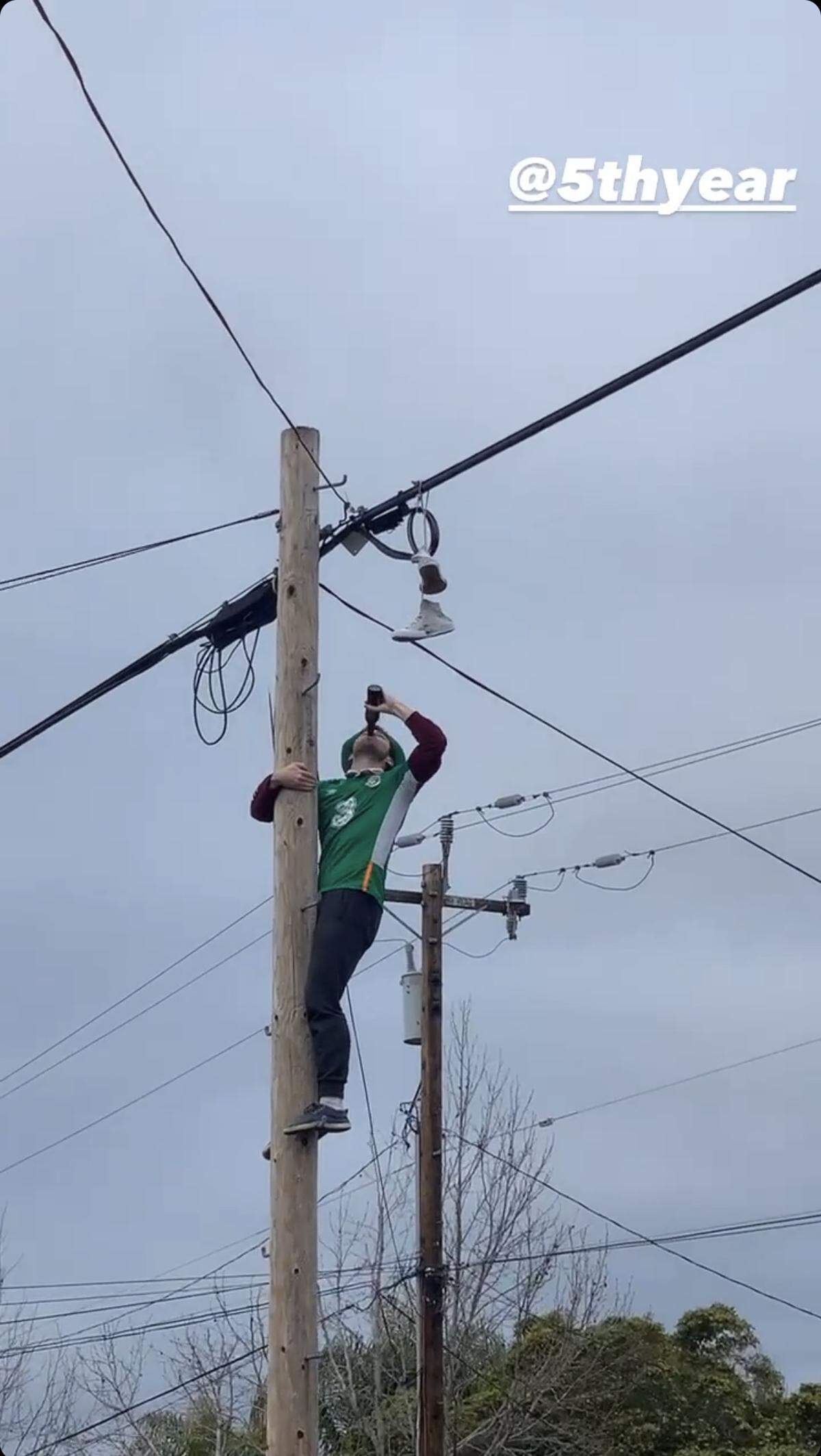 A man wearing green drinks a beer on a utility pole as a crowd cheers, part of a St. Fratty's Day celebration Saturday, March 13, 2021, amid the ongoing threat of the coronavirus pandemic.