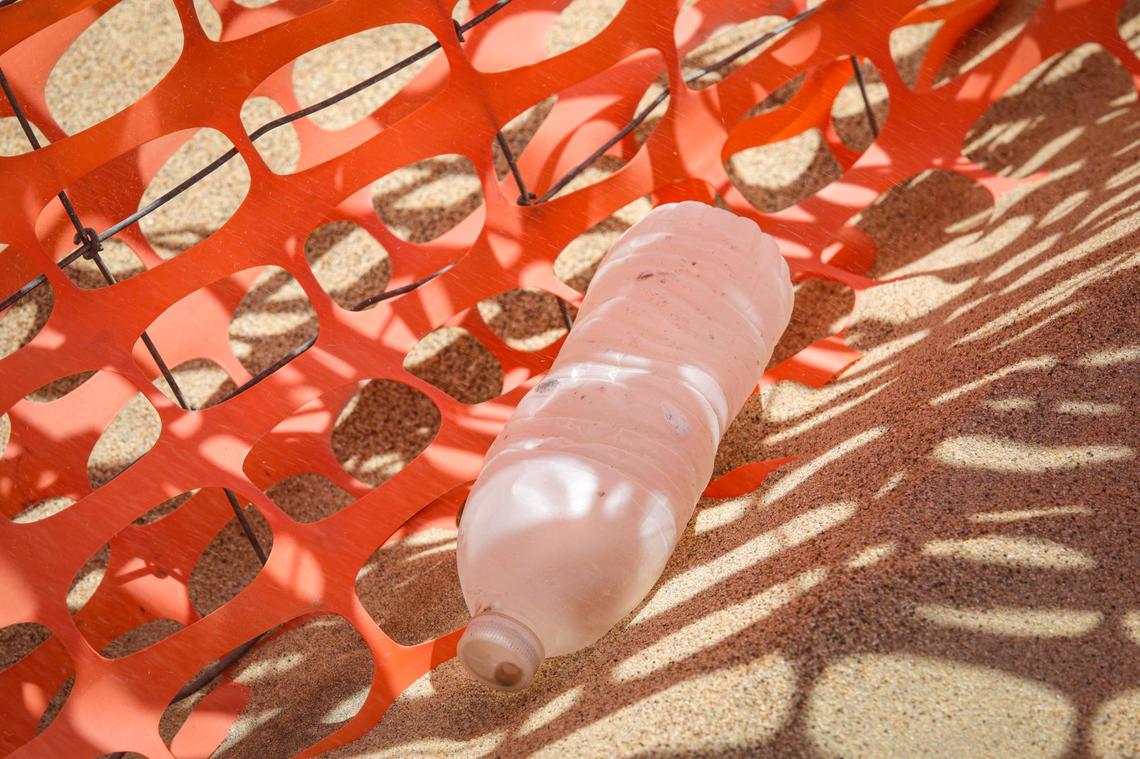 A formerly clear plastic water bottle has had the surface abraded by sand and is opaque, caught in a sand fence at the Oceano Dunes SVRA.