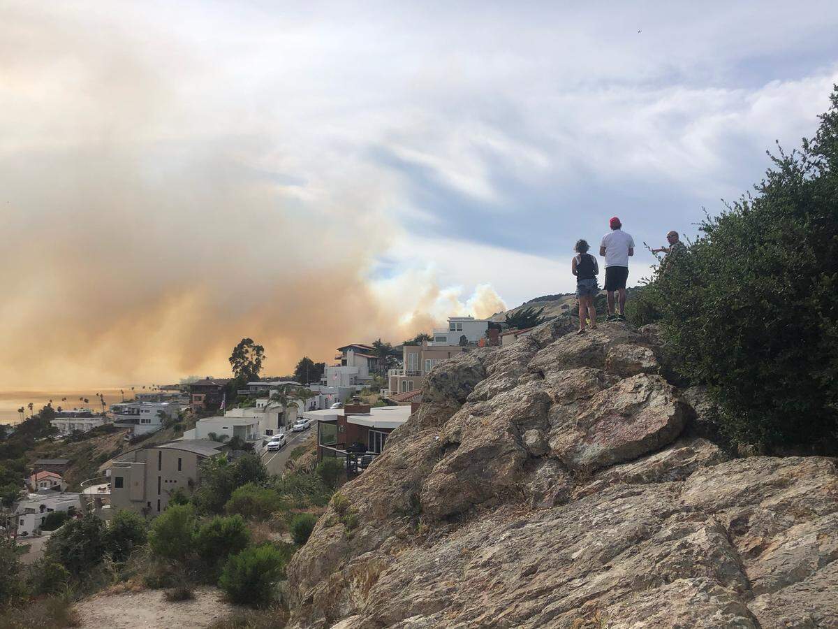 People stand on a cliff next to Boosinger Park on Wadsworth Avenue in Pismo Beach, looking at smoke from a nearby vegetation fire, on Monday, June 15, 2020.