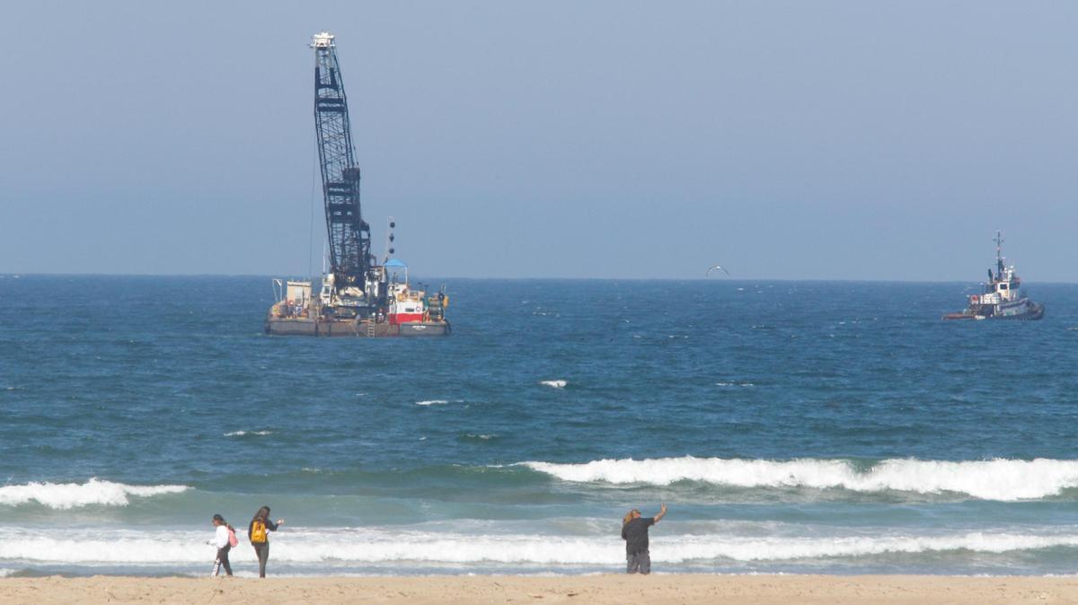 A crane on a barge is working to remove undersea pipeline in the Estero Bay north of Morro Rock.