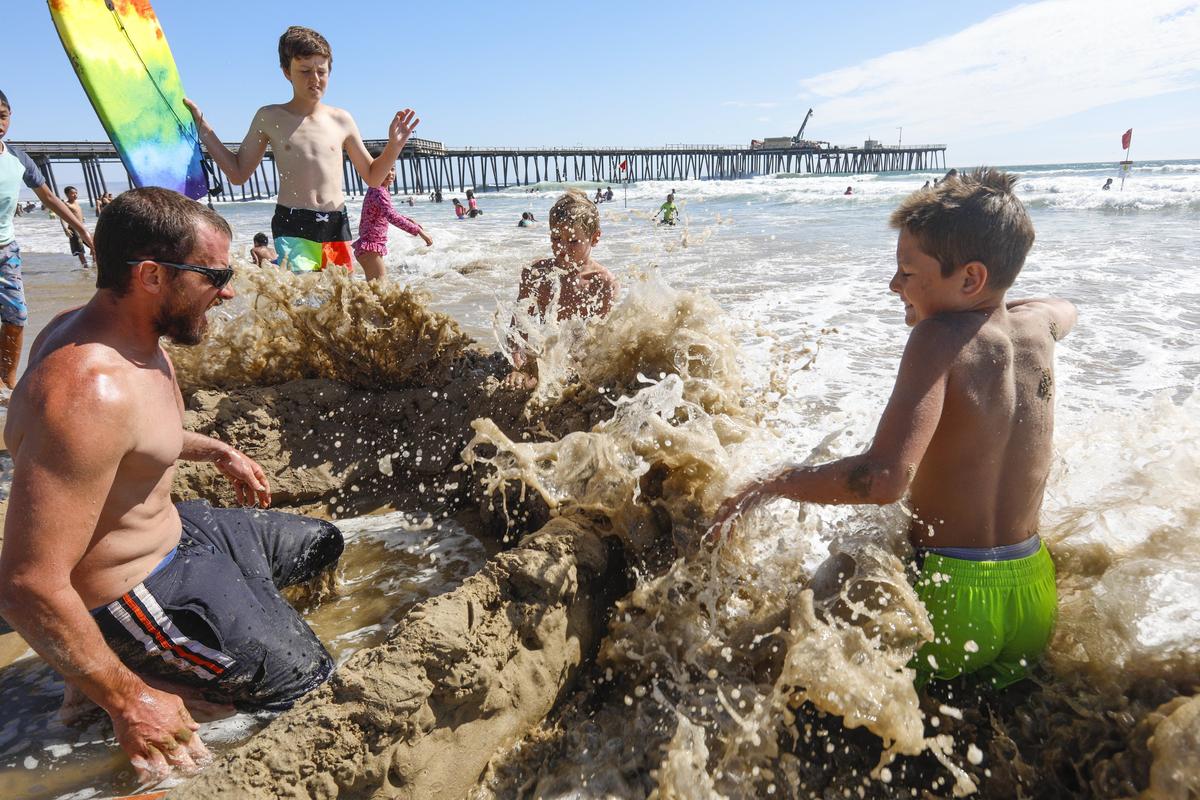 Working against the tide to save their sand fortress are Conor Sullivan and sons, from left, Cohen, 14; Caen, 10; and Calen, 12, of Clovis. Crowds flocked to Pismo Beach in July as hot weather swept the region.