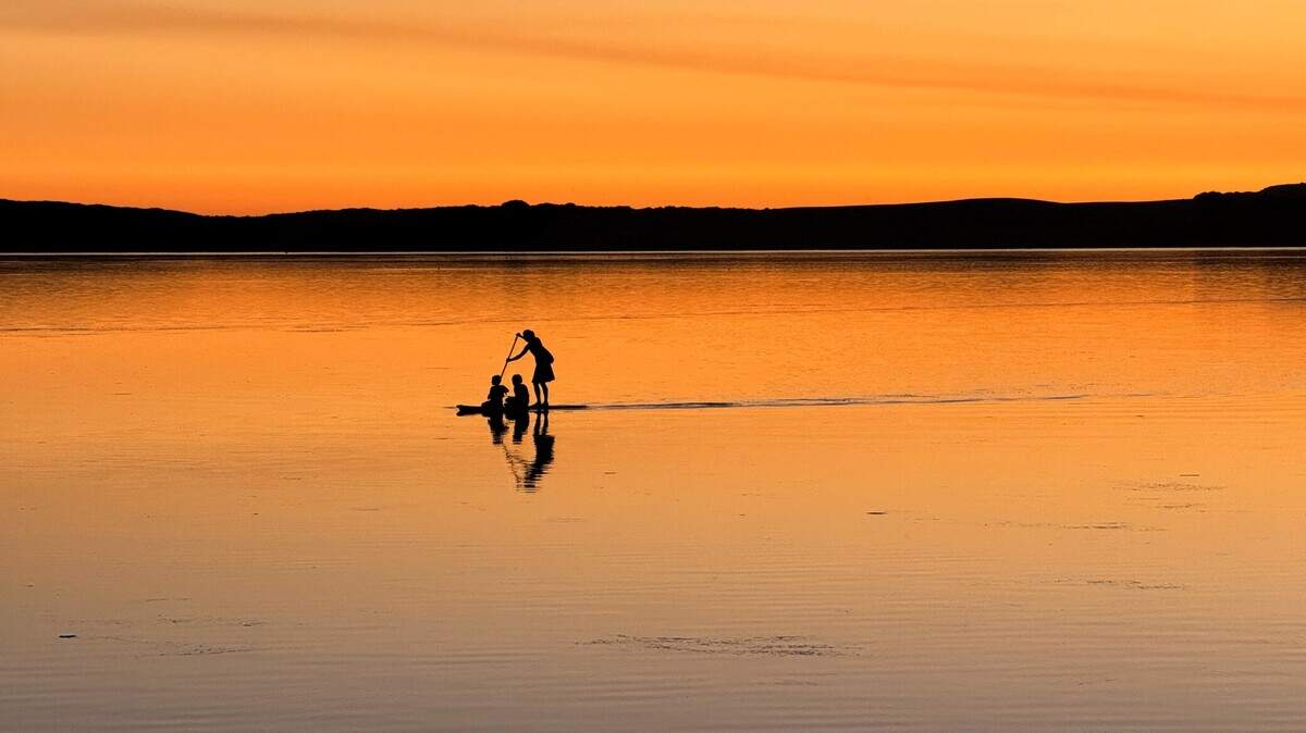 A paddleboarder with two kids crosses Morro Bay at sunset.