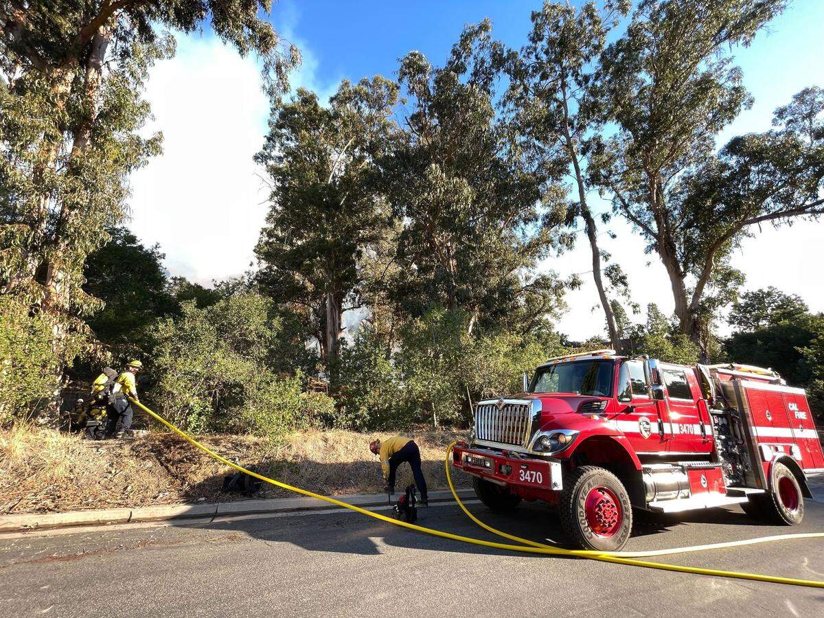 Cal Fire fighters use a fire hose to douse flames burning near San Luis Obispo High School on Monday, Oct. 30, 2023.