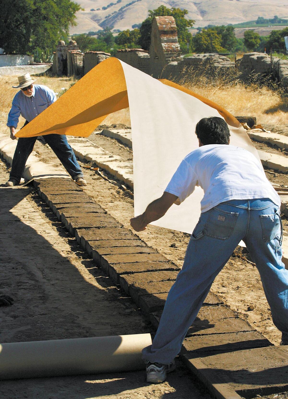 Freshly made adobe bricks are covered in paper and lightly sprinkled with water to prevent them from drying too fast and cracking. Rebuilding the earthquake ravaged Mission San Miguel on Aug. 28, 2006.