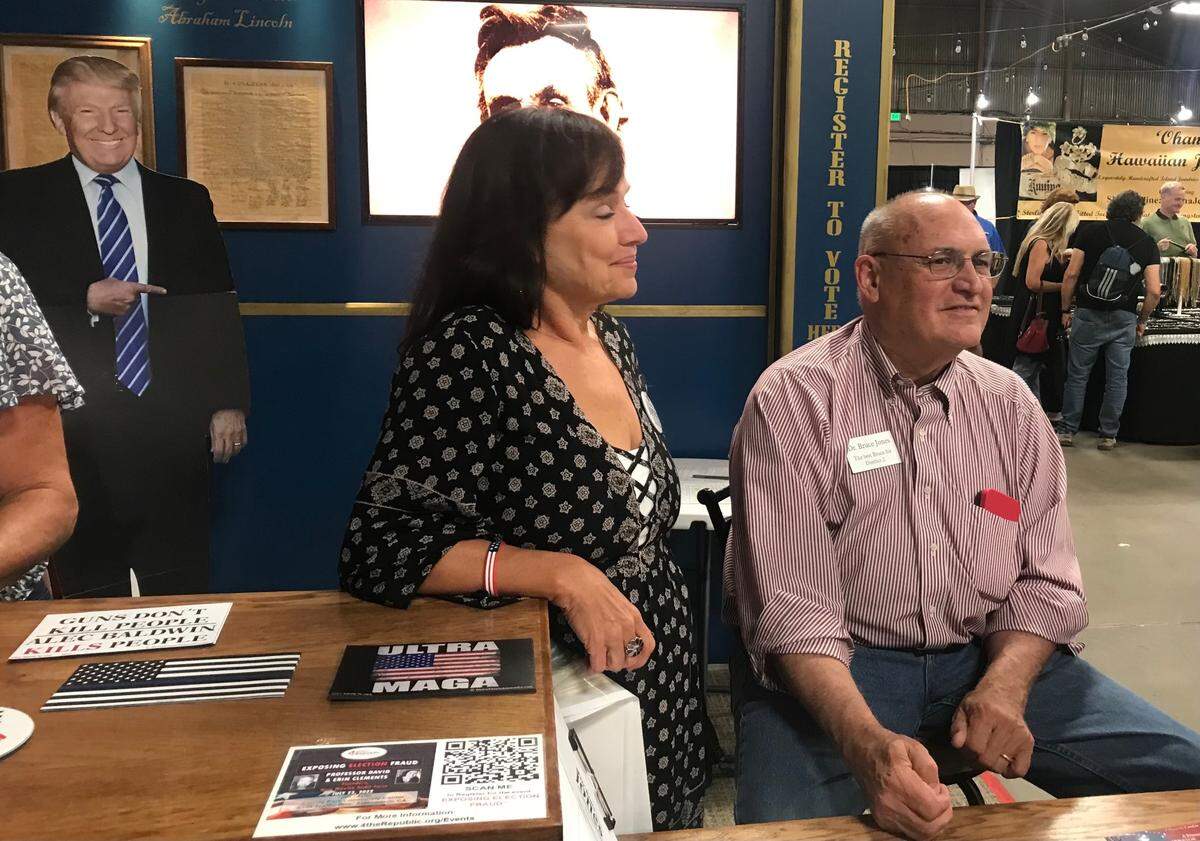Dr. Bruce Jones, right, a candidate for San Luis Obispo County supervisor, greets visitors to the Mid-State Fair in Paso Robles under the gaze of a Donald Trump cutout in the background.