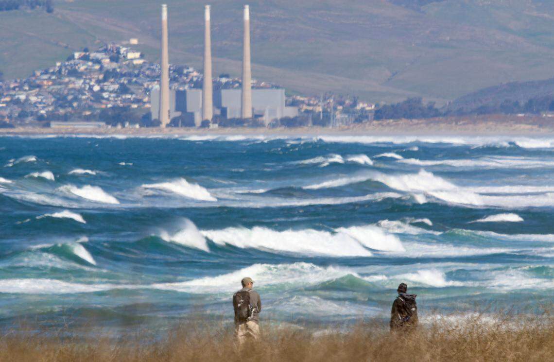 From the bluff trail south of Spooner’s Cove, hikers at Montana de Oro State Park watch the high surf in February 2020 with the mothballed Morro Bay Power Plant in the background.
