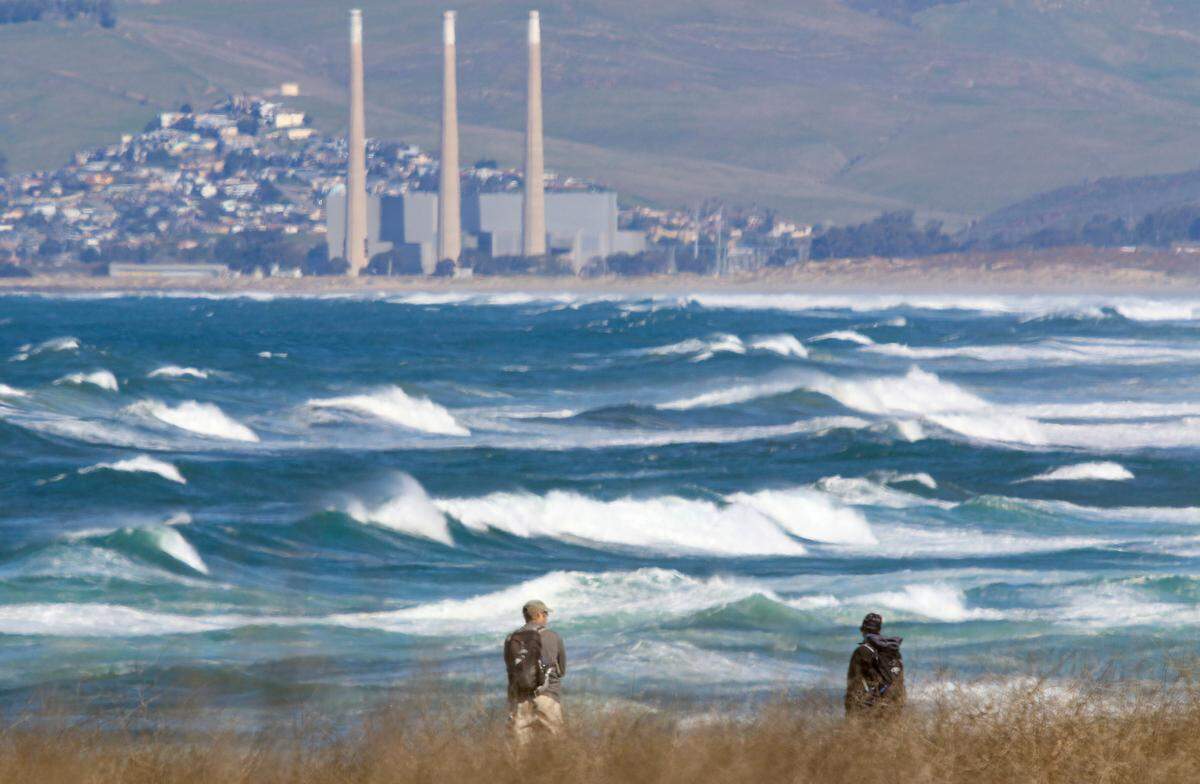 From the bluff trail south of Spooner’s Cove, hikers at Montana de Oro State Park watch the high surf in February 2020 with the mothballed Morro Bay Power Plant in the background.