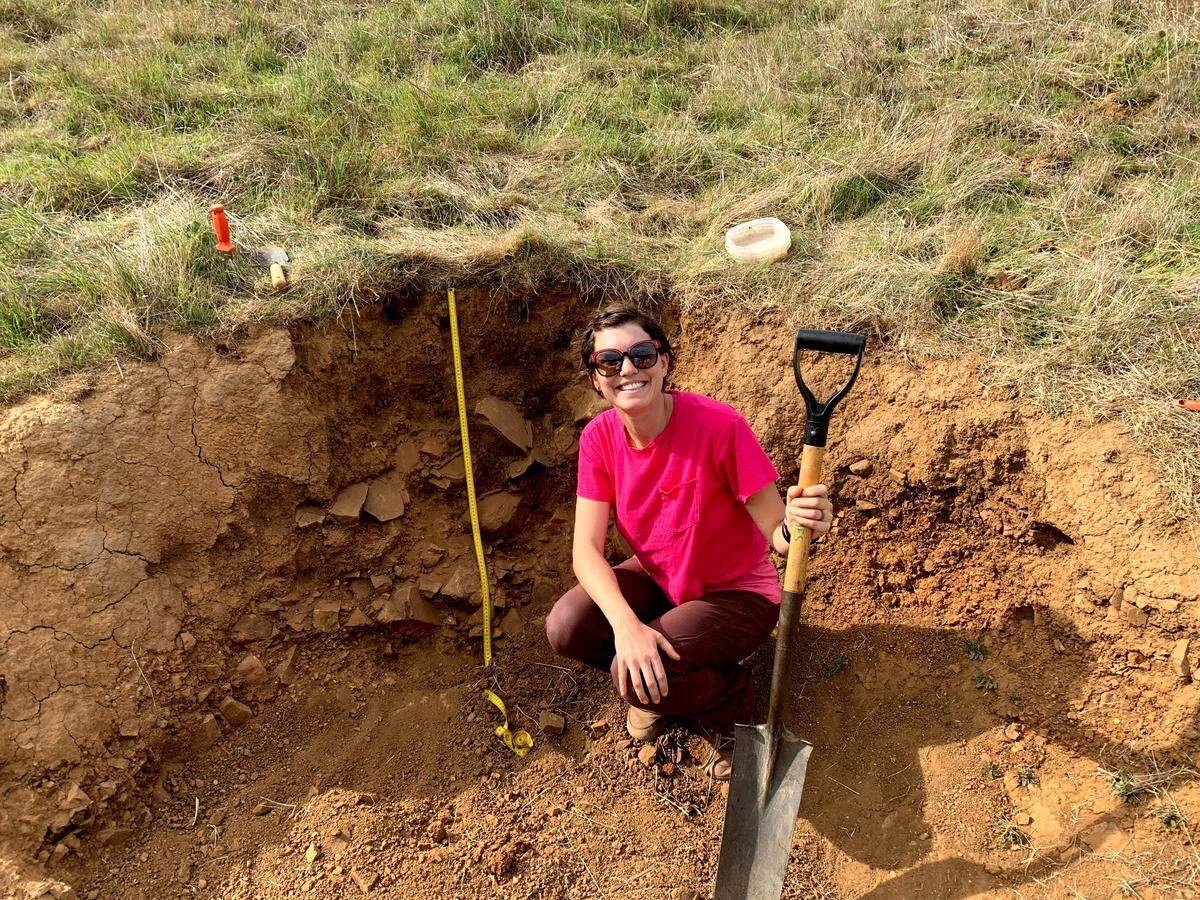 Person with a large smile crouching in a hole holding a shovel