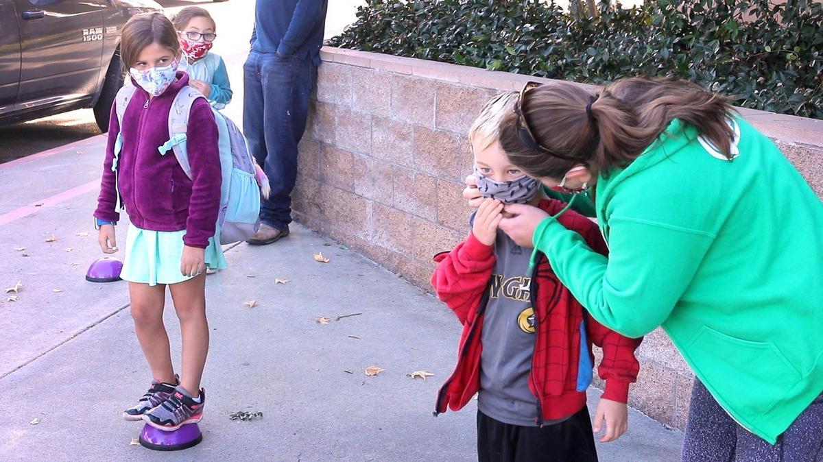Margaux O’Quest adjusts the mask of son Dylan, 6, before the students leave for class. Transitional Kindergarten through second grade students attend in-person classes at San Gabriel Elementary School in Atascadero for the first time since March. The students are some of the first in the county at a public school to return to classrooms after the coronavirus pandemic caused schools to shift to virtual-only learning.