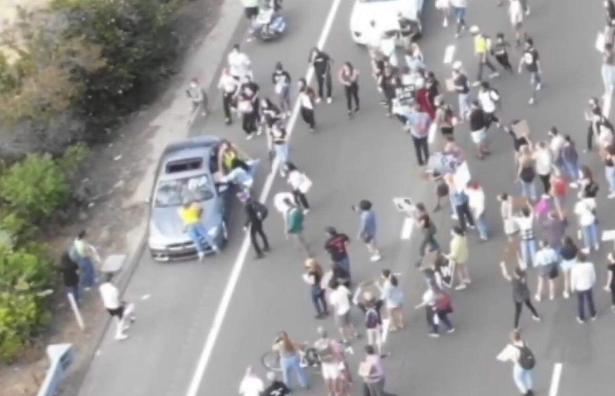 A screen shot from the drone video shows Sam Grocott, in yellow, on the hood of the silver BMW. The motorist drove into Grocott during protesters’ blockade of Highway 101 on July 21, 2020.