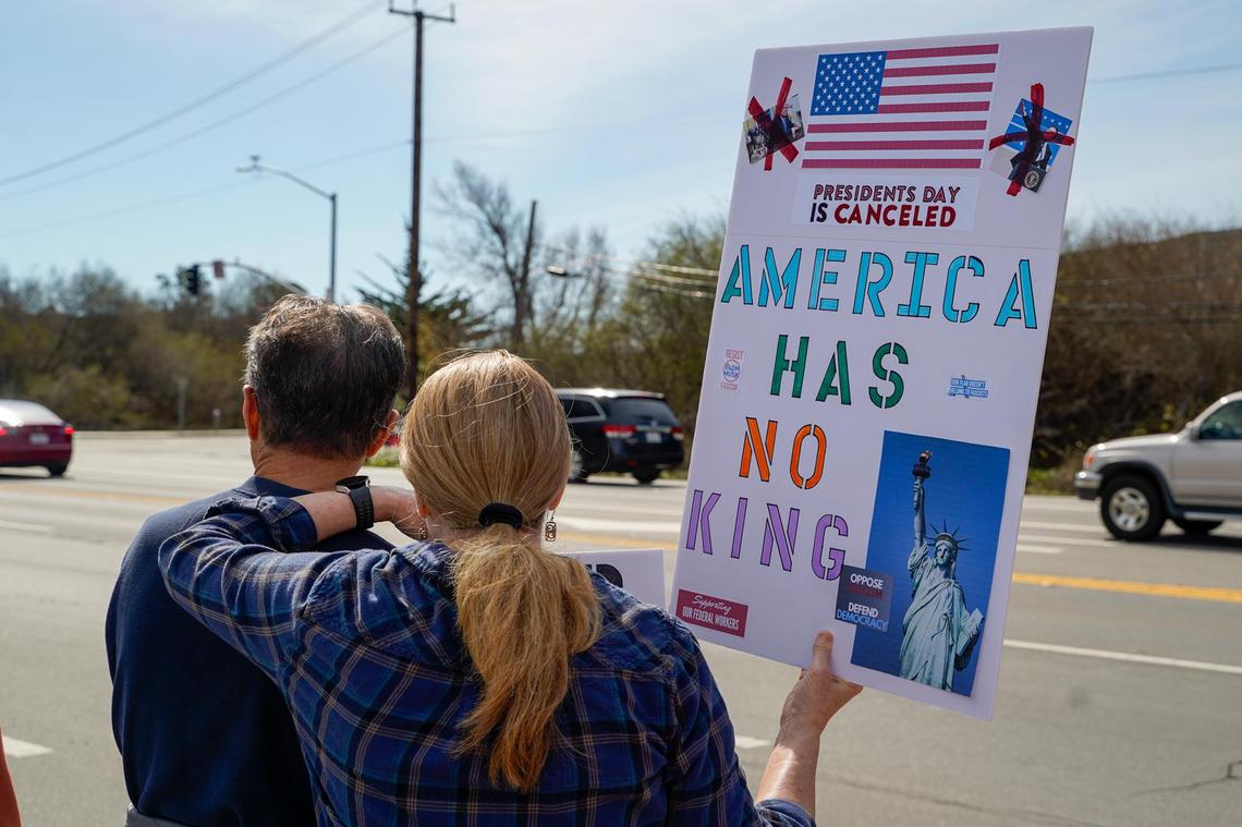Protesters hold signs and chant to show their opposition to the policies of Donald Trump’s second term in office and Elon Musk’s Department of Governmental Efficiency, on Los Osos Valley Road on Monday, Feb. 17, 2025.