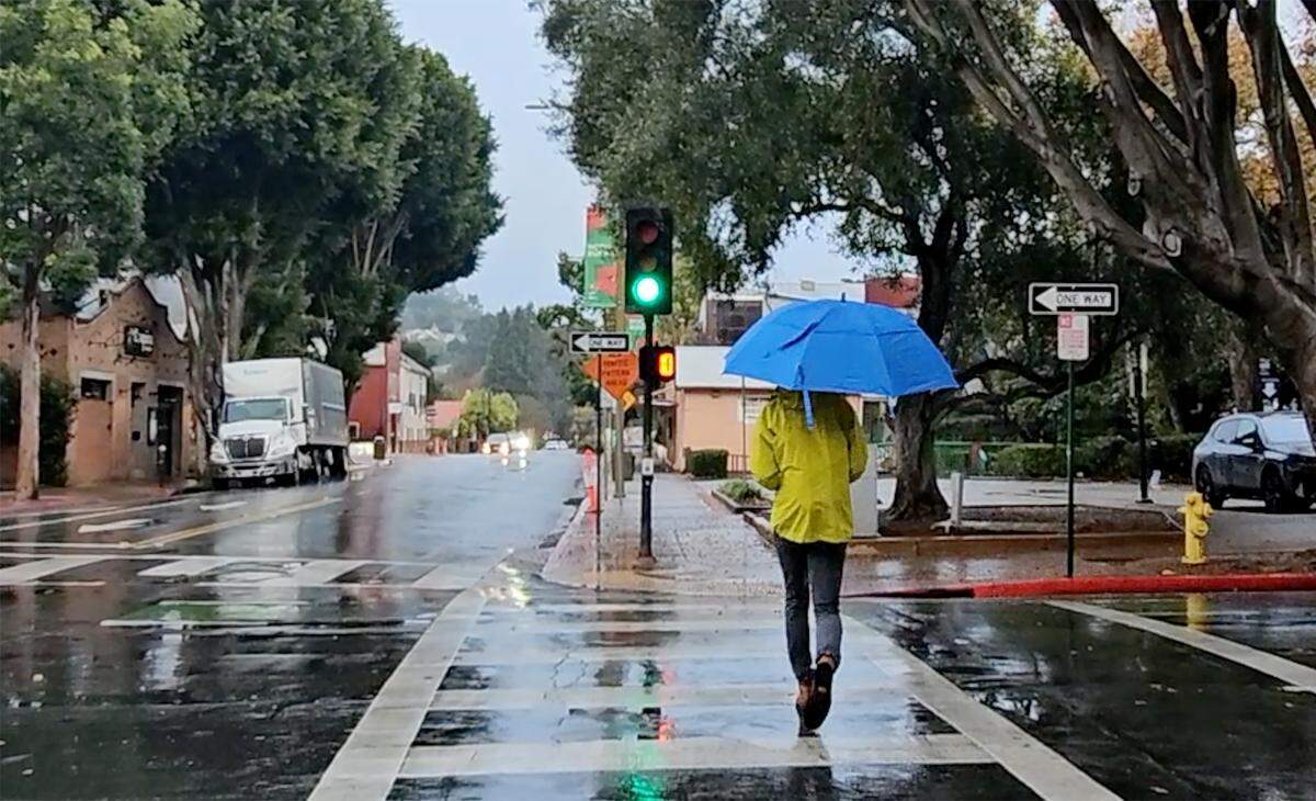 A man with an umbrella crosses Higuera Street as light rain hit San Luis Obispo on Thursday, Dec. 12, 2024.