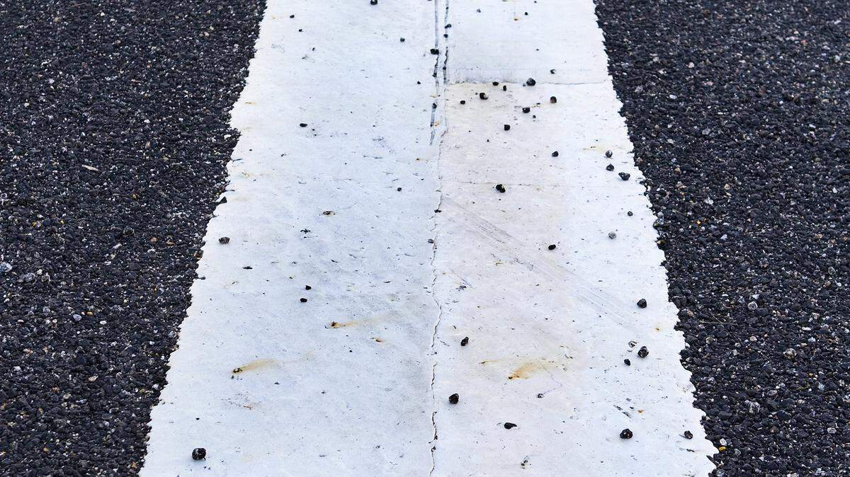 An arrow marker in the newly paved section of Highway 1 is littered with loose pieces of the new larger paving aggregate.