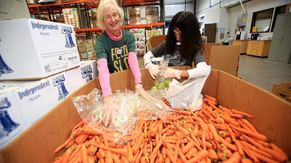 SLO Food Bank volunteers work stuffing plastic bags with food for needy persons. Pamela Werth and longtime volunteer Joan Barbieri.