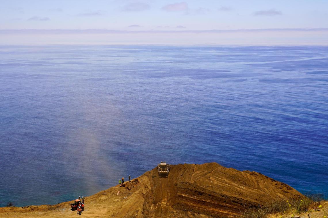 A bulldozer operated by Caltrans repair crews pushes debris off the edge of Regent’s Slide and into the Pacific Ocean more than 600 feet below, pictured Thursday, July 17, 2025. Regent’s Slide closed Highway 1 around 27 miles north of the San Luis Obispo-Monterey county line in February 2024.