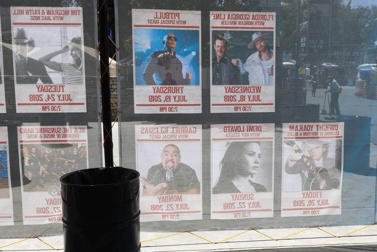 Posters reflect the sun on a shade screen as a groundskeeper sweeps at right. Garbage at the Mid State fairgrounds does not stay in one place long. Collection cans are in line of sight almost everywhere as are crews are sweeping and hauling. David Middlecamp 7-20-2018