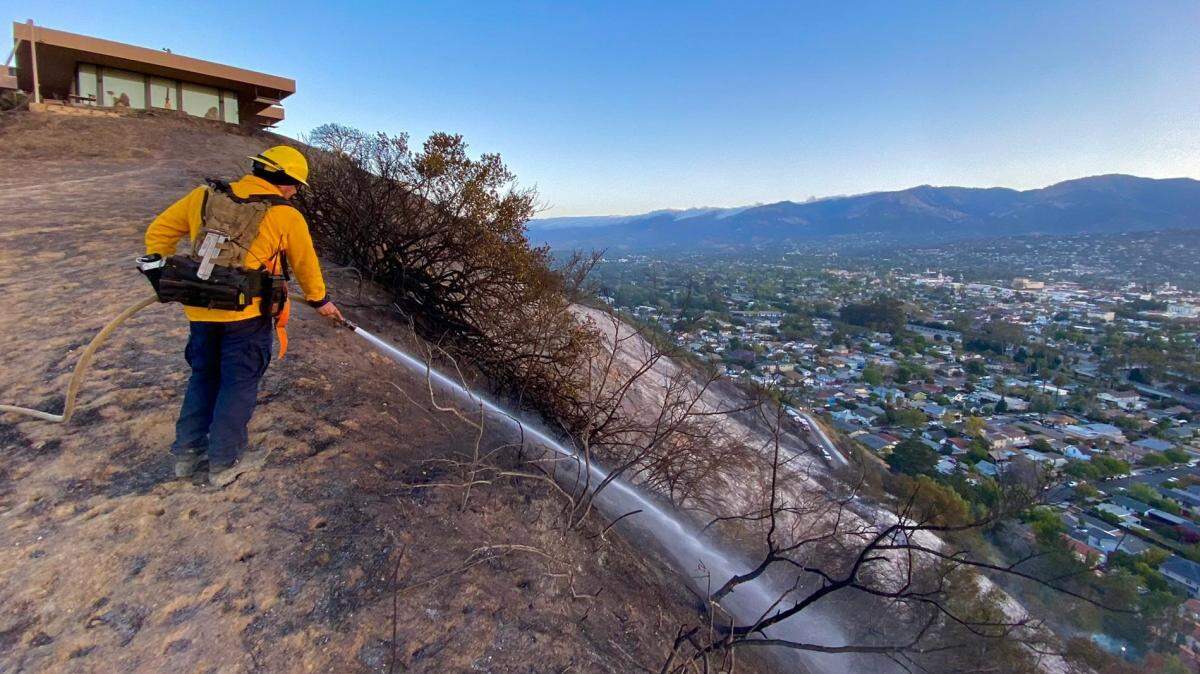 A firefighter hoses down the smoldering hillside on the morning of Friday, May 21, 2021, after the Loma Fire burned about 10 acres and damaged two buildings in Santa Barbara.