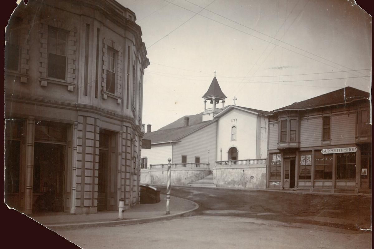 Mission San Luis Obispo is seen from the corner of Monterey and Chorro streets between 1880 and 1920. At the left of the photo is the Lasar Building or Mission Garage, originally built around 1880 and housed the print shop for the Morning Tribune newspaper in the 1880s. At the right of the photo is a real estate office and gunsmith.