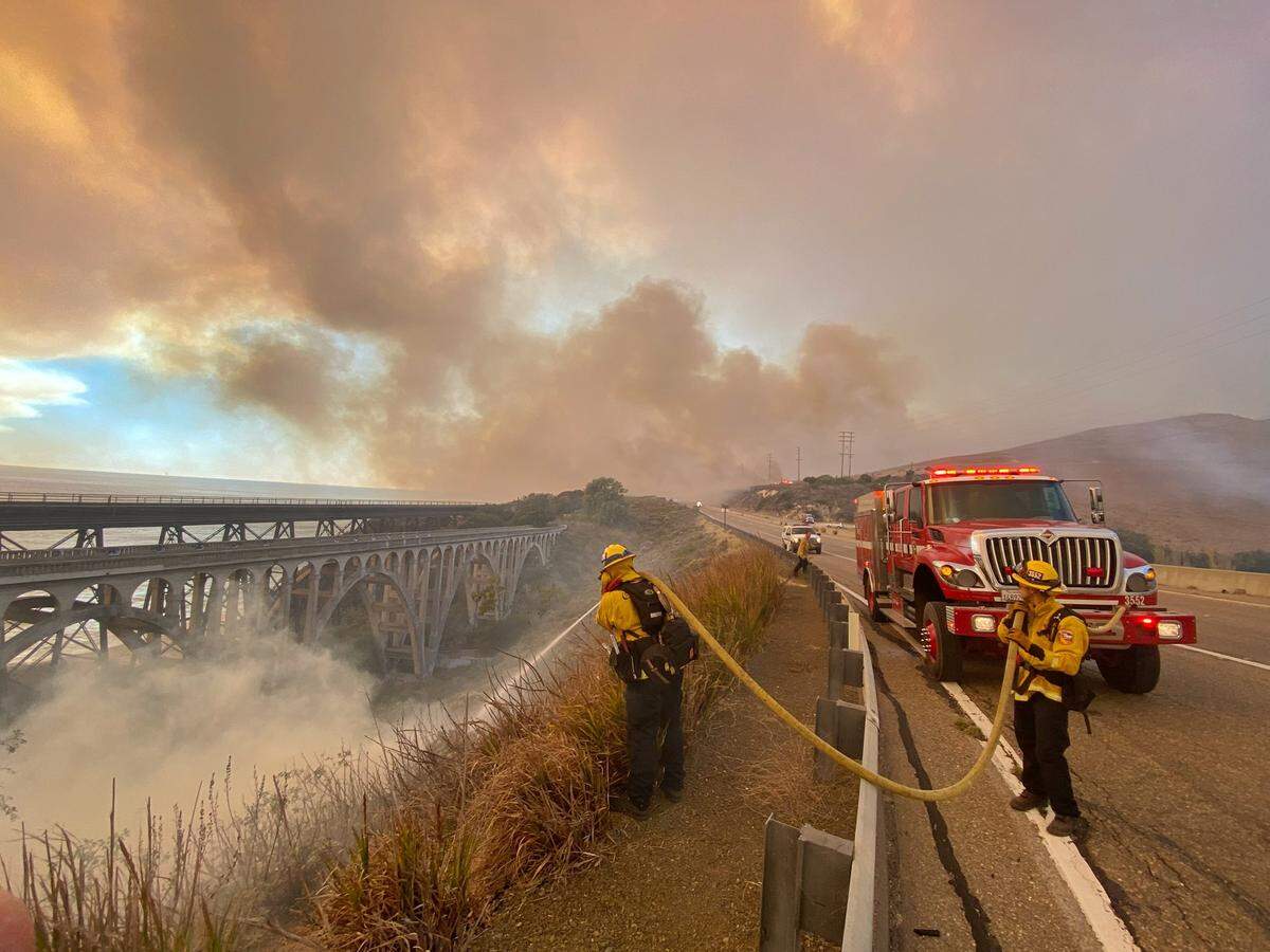 Firefighters extinguish flames from the Alisal Fire along Highway 101 southbound at Vista Point, north of Refugio State Beach on Tuesday afternoon.
