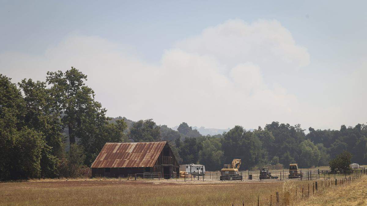 A smoke plume rises behind a barn on Hi Mountain Road above Lopez Lake, seen here on Aug. 8, 2025. As of the morning of the eighth day of the Gifford Fire, 3,431 firefighters were working in shifts on the 99,232-acre blaze.