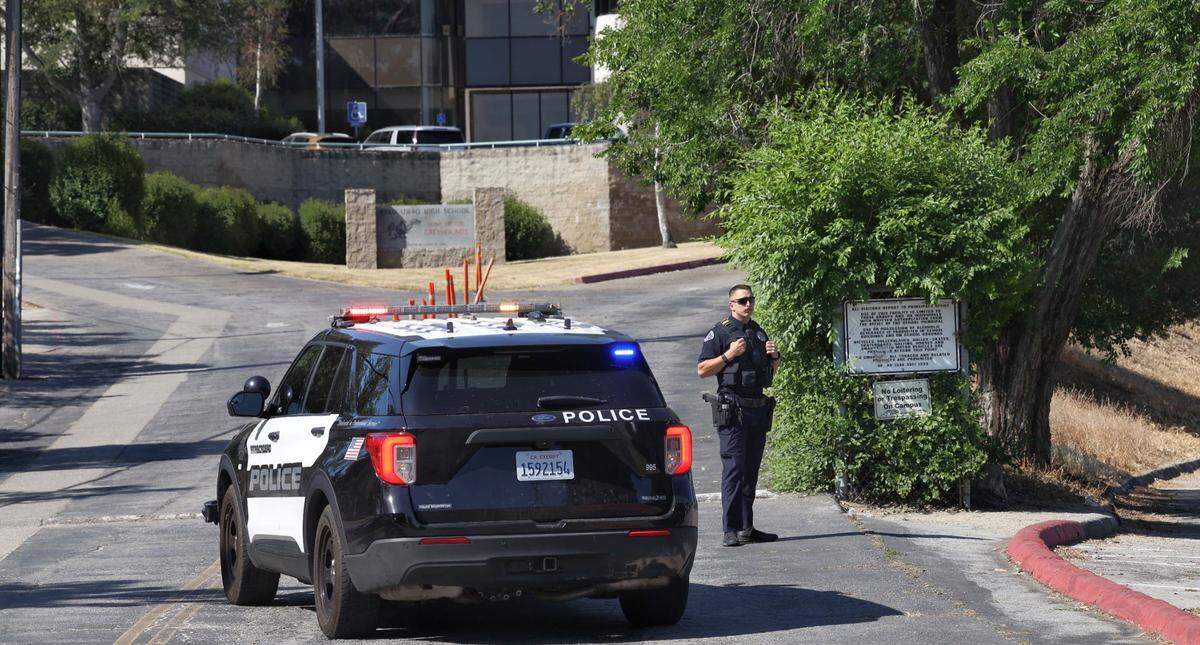 An Atascadero Police Department officer stands next to a patrol car at the entrance of Atascadero High School on Thursday, May 26, 2022. Students were evacuated and the campus was placed on lockdown due to a safety threat.