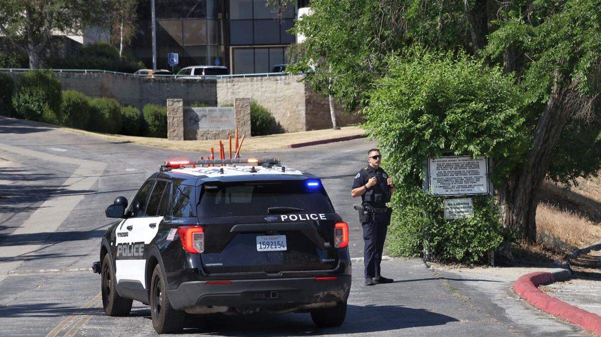 An Atascadero Police Department officer stands next to a patrol car at the entrance of Atascadero High School on Thursday, May 26, 2022. Students were evacuated and the campus was placed on lockdown due to a safety threat.