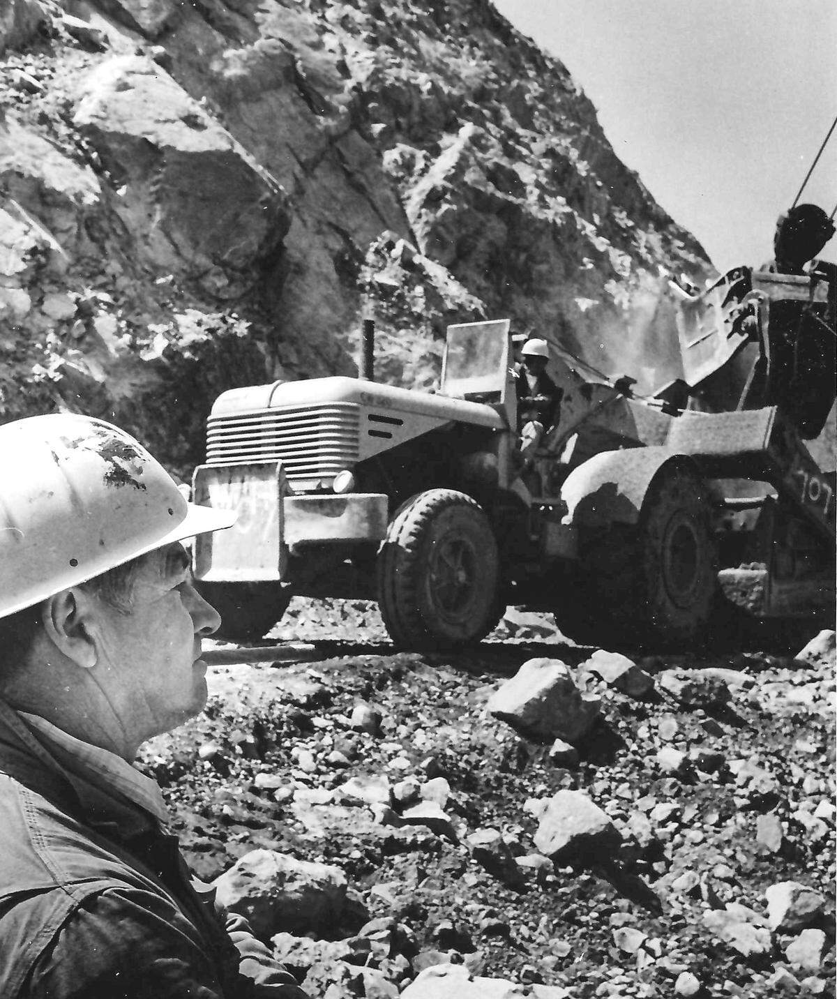 EARTHMOVER - After boulders and earth are losened by blasting, huge caryalls like this one carve the new highway bed from the crumbling mountianside. Looking on is oiler Bill Huntington. Story published May 22, 1971 on the construction of Highway 166.