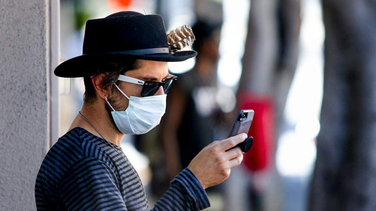 A masked Adam Marz checks his phone in downtown San Luis Obispo near the FedEx print and ship office on Chorro Street. County complaints include allegations of violations of mask policies.