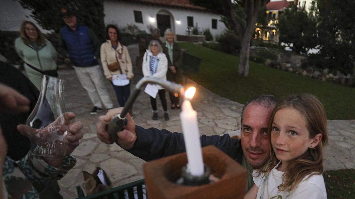 Nachshon Margalit and daughter Ava,8, light the shamash, or helper candle, used to light the others on the menorah. About a dozen people gathered in front of Mission San Luis Obispo to light the menorah on the second night of Hanukkah on Dec. 15, 2025.