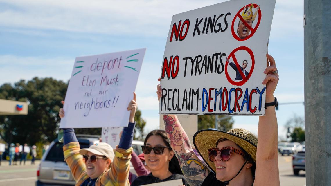 Protesters hold signs and chant to show their opposition to the policies of Donald Trump’s second term in office and Elon Musk’s Department of Governmental Efficiency, on Los Osos Valley Road on Monday, Feb. 17, 2025.