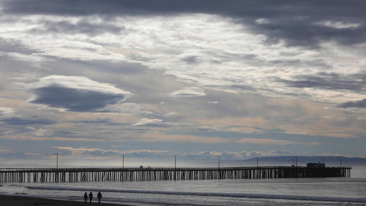 Three people take a walk at Avila Beach near the pier as overcast skies break up on Friday, Dec. 22, 2023, following a week of storms.