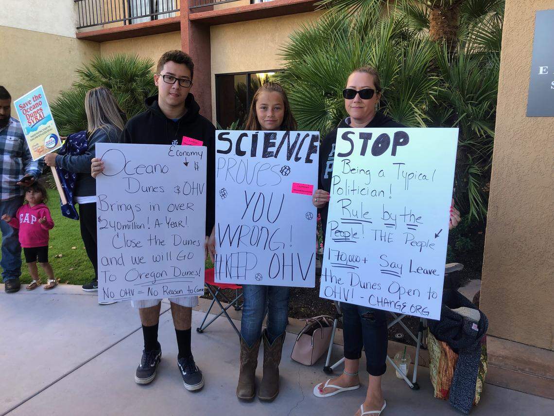 People with signs outside the Embassy Suites in San Luis Obispo before the start of the California Coastal Commission meeting on Thursday.
