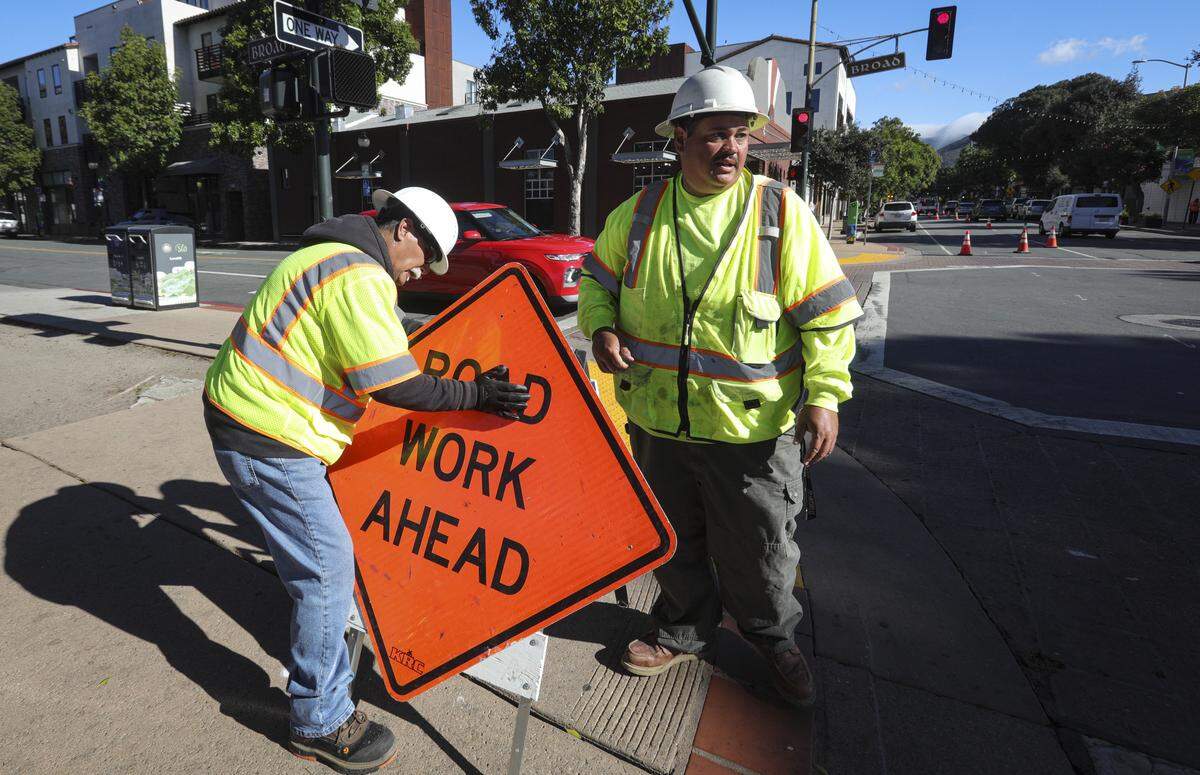 Gabriel Grandado, left and Isreal (declined to give last name) put up construction sign at corner of Marsh and Broad Streets in downtown San Luis Obispo on Oct. 27, 2025.