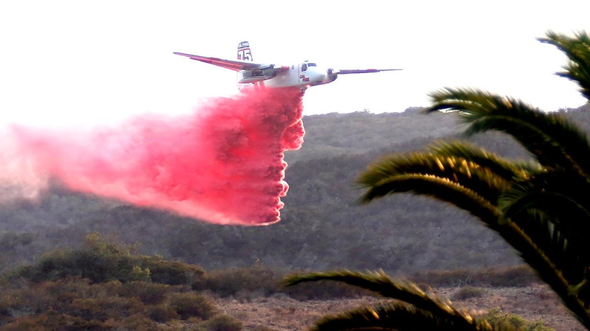 An air tanker drops fire retardant on the fire behind the hillside. Emergency crews are at the scene of a reported vegetation fire on the Irish Hills south of San Luis Obispo, near the Home Depot and Costco shopping centers.