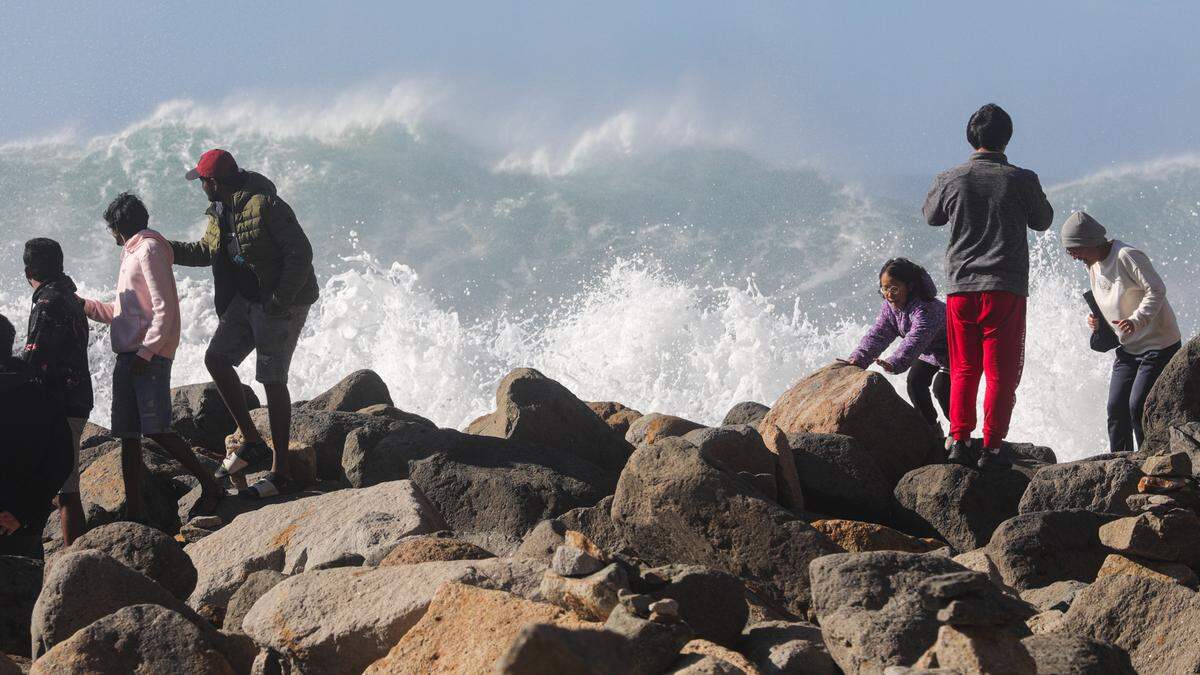 A high surf advisory brings wave watchers to the Morro Bay breakwater near Morro Rock on Tuesday, Dec. 27, 2022. A sneaker set of higher than average waves convinced spectators to move back. This wave crashed on previously dry rocks as the tide was rising.