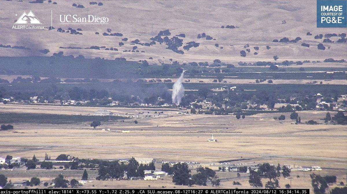 A helicopter makes a water drop on a fire that burned several outbuildings near the Paso Robles Municipal Airport on Monday, Aug. 12, 2024.
