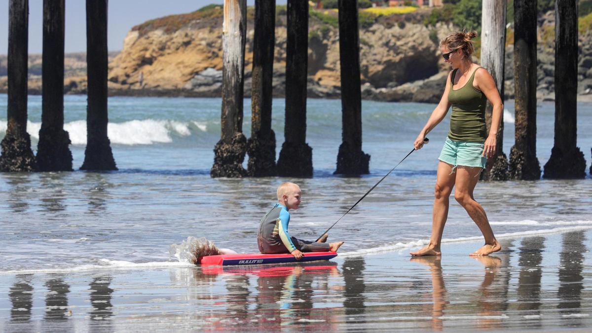 Amy Valley tows son Jed, 3, in the surf at Cayucos. Families enjoyed the cool weather at the beach as a heat wave is forecast for the upcoming days.