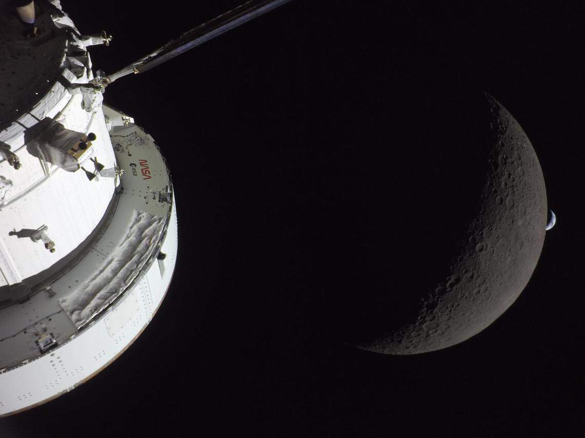 NASA’s Orion spacecraft captures the moon and the Earth in one frame during the Artemis II crew’s deep space journey at 6:42 p.m. ET April 6, 2026, on the sixth day of the mission. The right side of NASA’s Orion spacecraft is seen lit up by the sun. A waxing crescent moon is visible behind it. And then, a crescent Earth, tiny compared to the moon, is about to set below the moon’s horizon on the right.