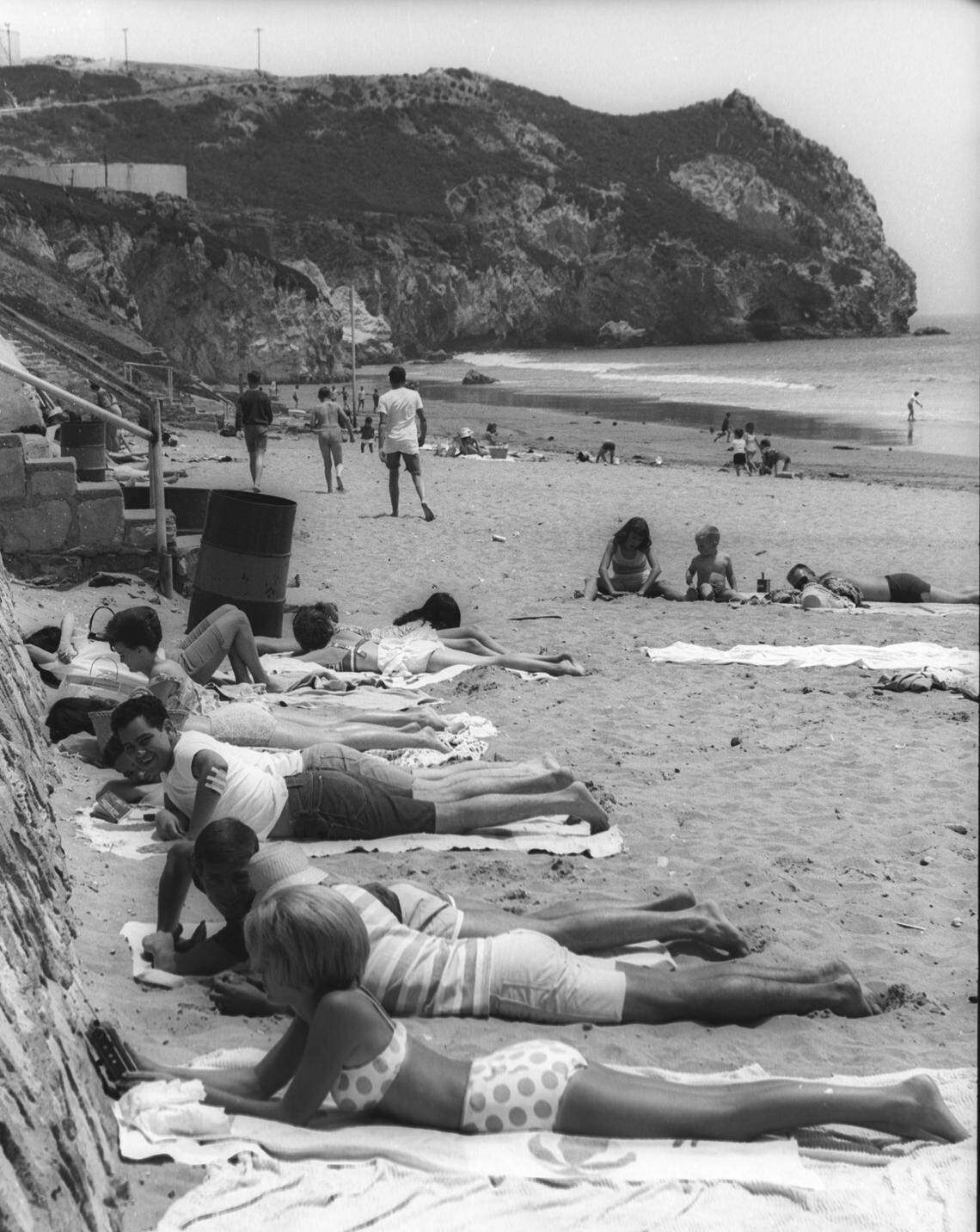 School out and crowds came to Avila Beach June 16, 1964 Sunbathers are0 next to the wall listening to transistor radio, oil tanks in background