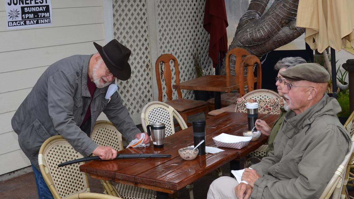 Mike Miller uses a windshield wiper to whisk water from a heavy drizzle off a table at the Back Bay Cafe in Baywood Park on Saturday as Jack and Gay McNeal look on.