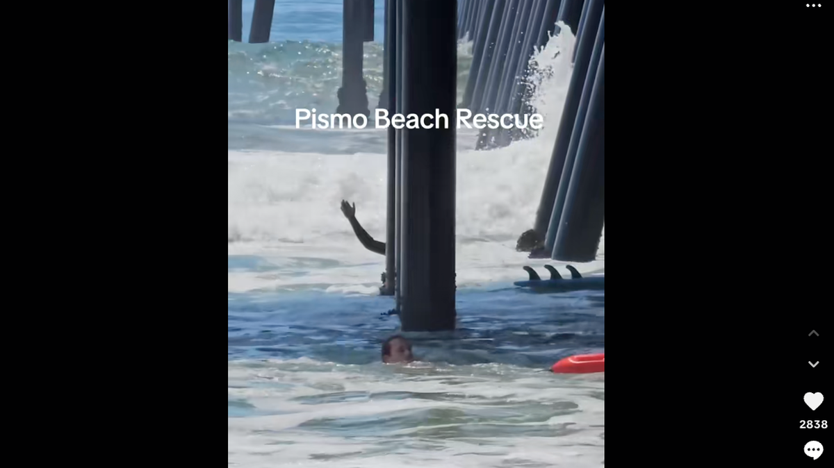 A surfer stuck alongside a piling of the Pismo Beach Pier waves for help as a lifeguard responds on Tuesday, Aug. 12, 2025, a TikTok video posted by user gallito894 shows.